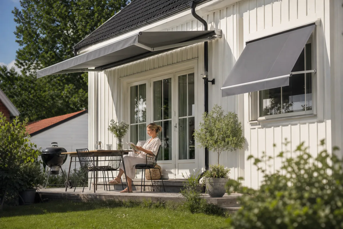 Prisv&auml;rd &ouml;ppen terrassmarkis och enkel f&ouml;nstermarkis monterade p&aring; fasaden till ett svenskt villahus en solig dag