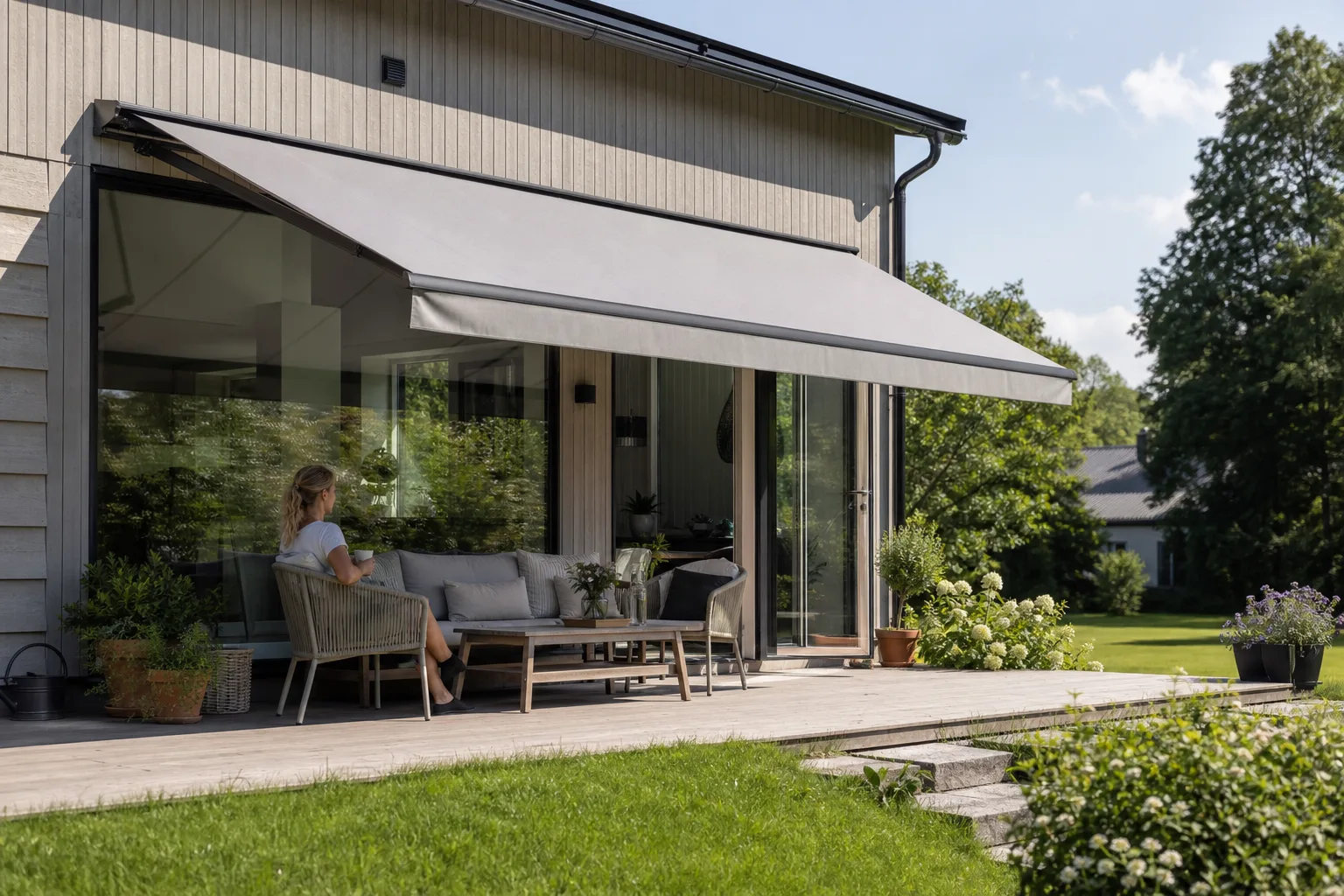 Svenskt hus en solig sommardag med en utfälld markis som skuggar fönstret och sittgruppen på terrassen