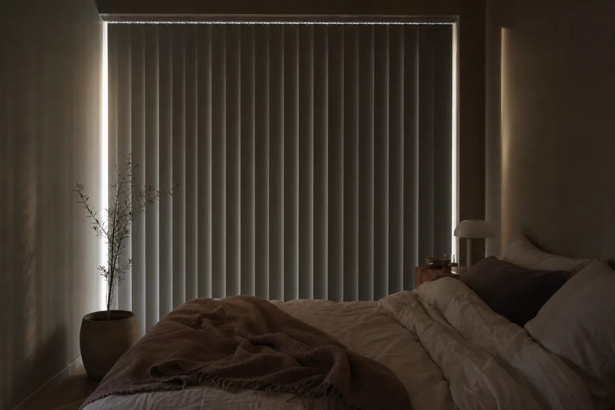 Ett svenskt sovrum tidigt p&aring; morgonen med m&ouml;rkl&auml;ggande lamellgardiner nedfällda &ouml;ver ett brett f&ouml;nster