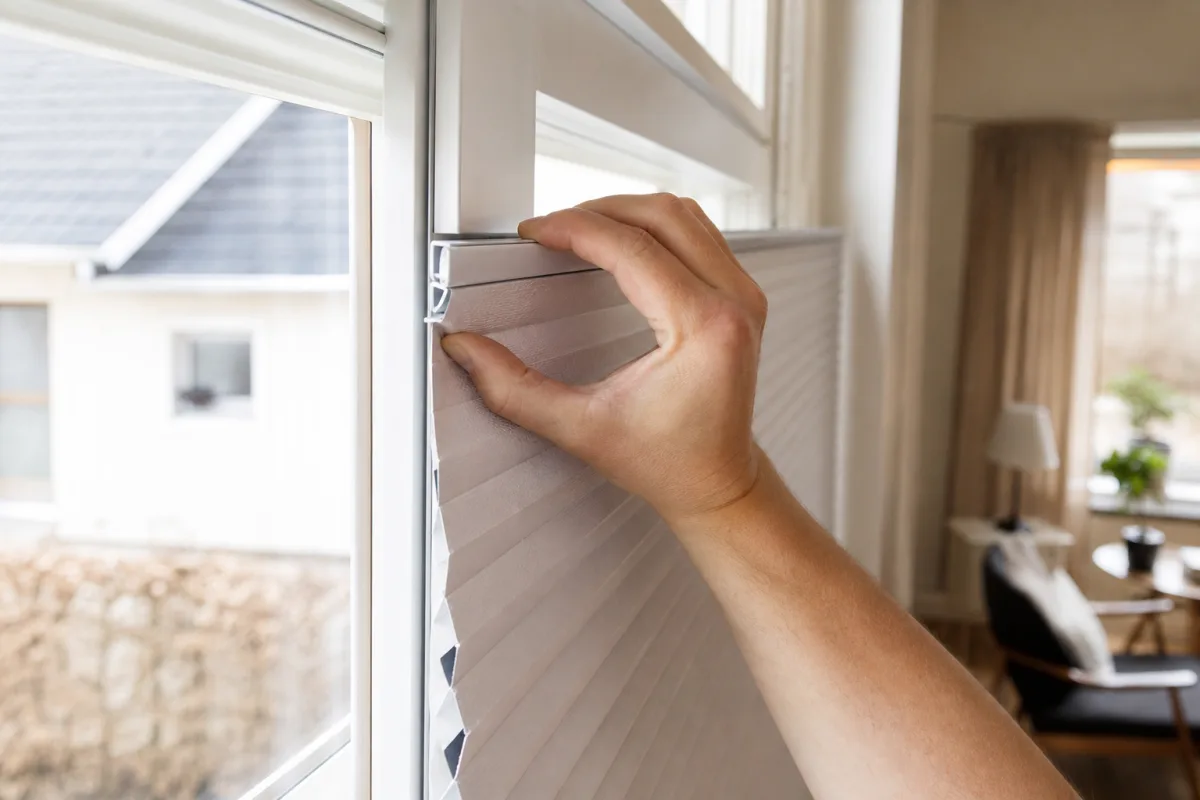 En hand kl&auml;mmer fast en Perfect Fit-ram med pliss&eacute;gardin direkt i ett PVC-f&ouml;nster utan borrning